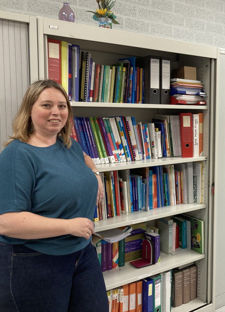 taalcoördinator staand naast boekenkast