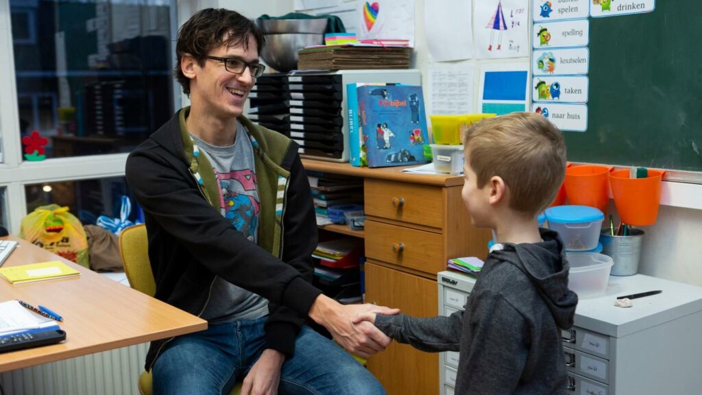 Een leraar verwelkomt een leerling in zijn klas